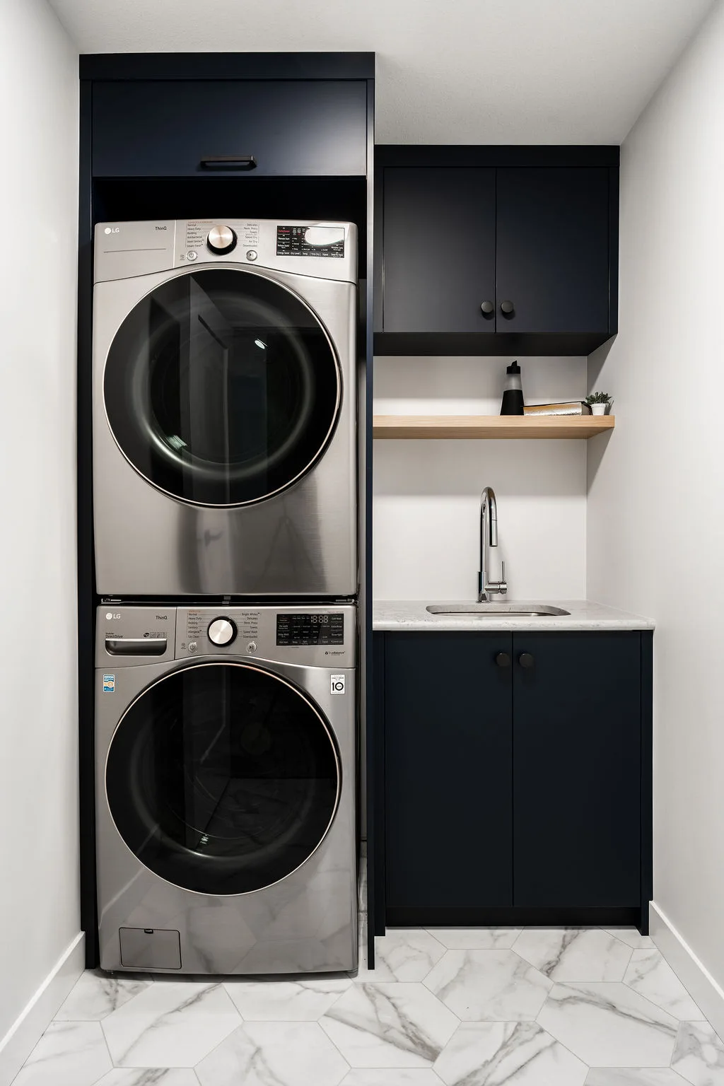 axium-interiors-saskatoon-laundry-room-stacked-stainless-steel-washing-machine-with-sink-area-DSC08260-HDR Walkout basement with dark cabinetry and gold accents, bright and spacious with floor to ceiling windows